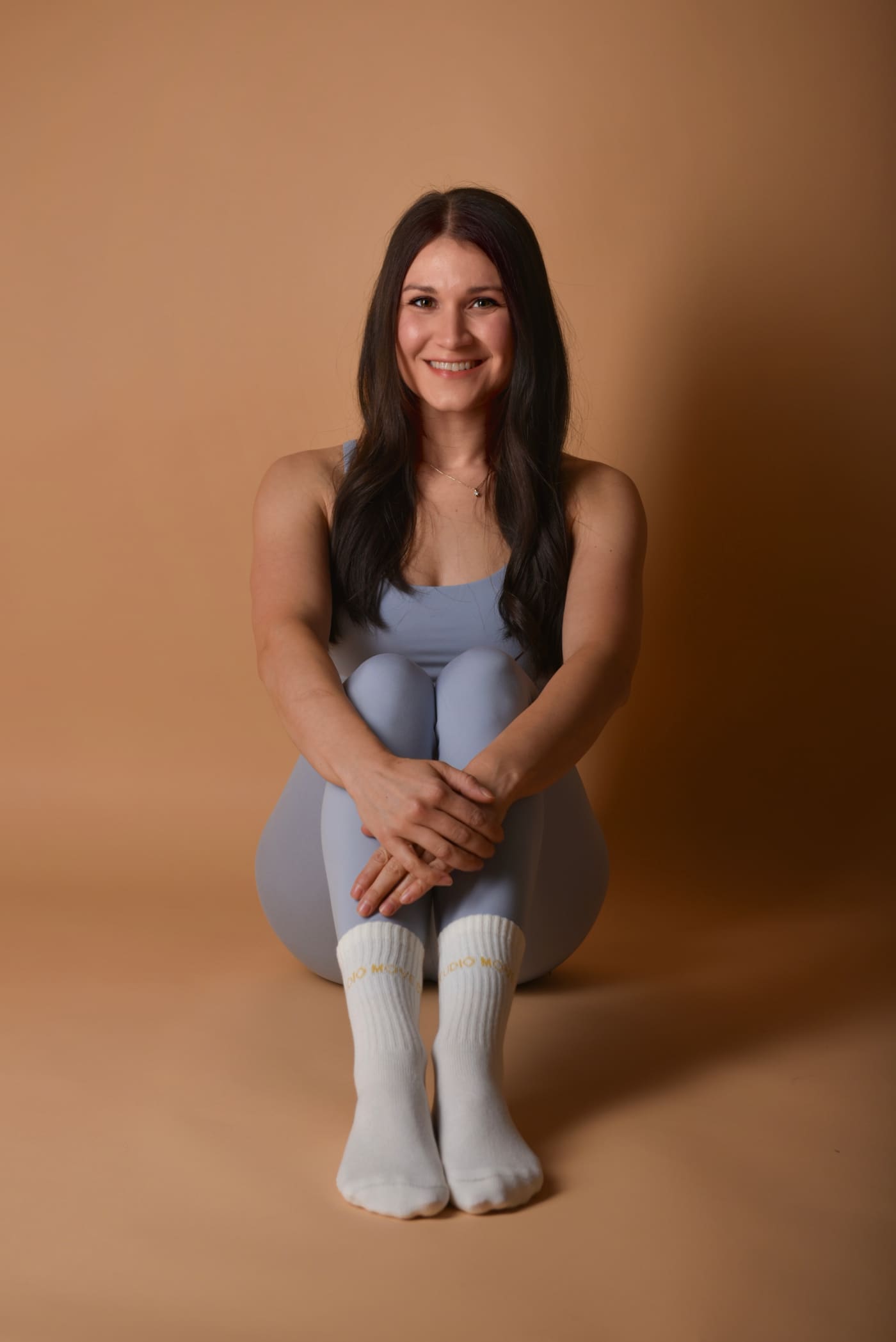 Aylin, Trainerin von Lini Mama Fitness, sitzt lächelnd vor warmem Hintergrund