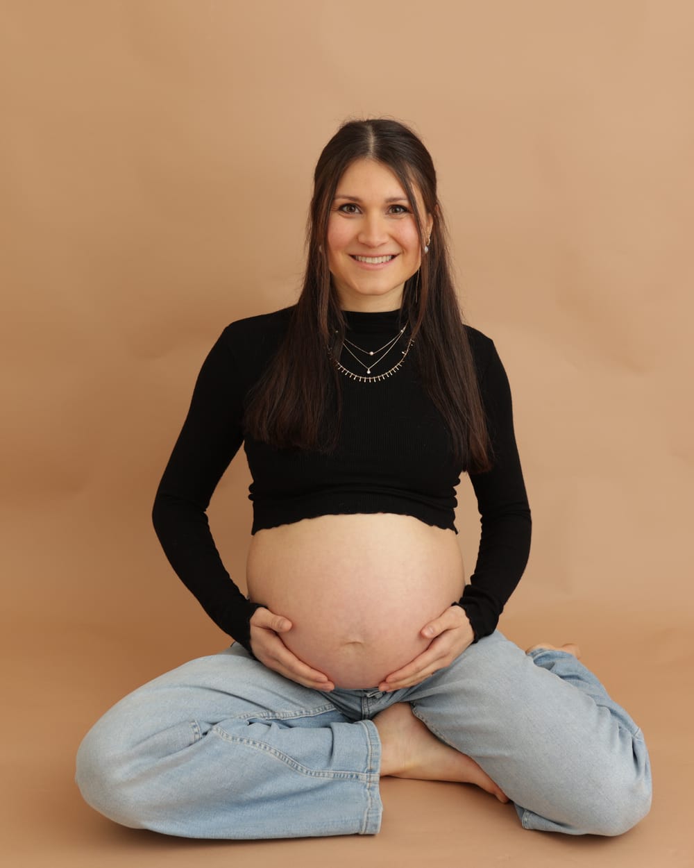 Aylin, schwanger, sitzt lächelnd und hält ihren Babybauch