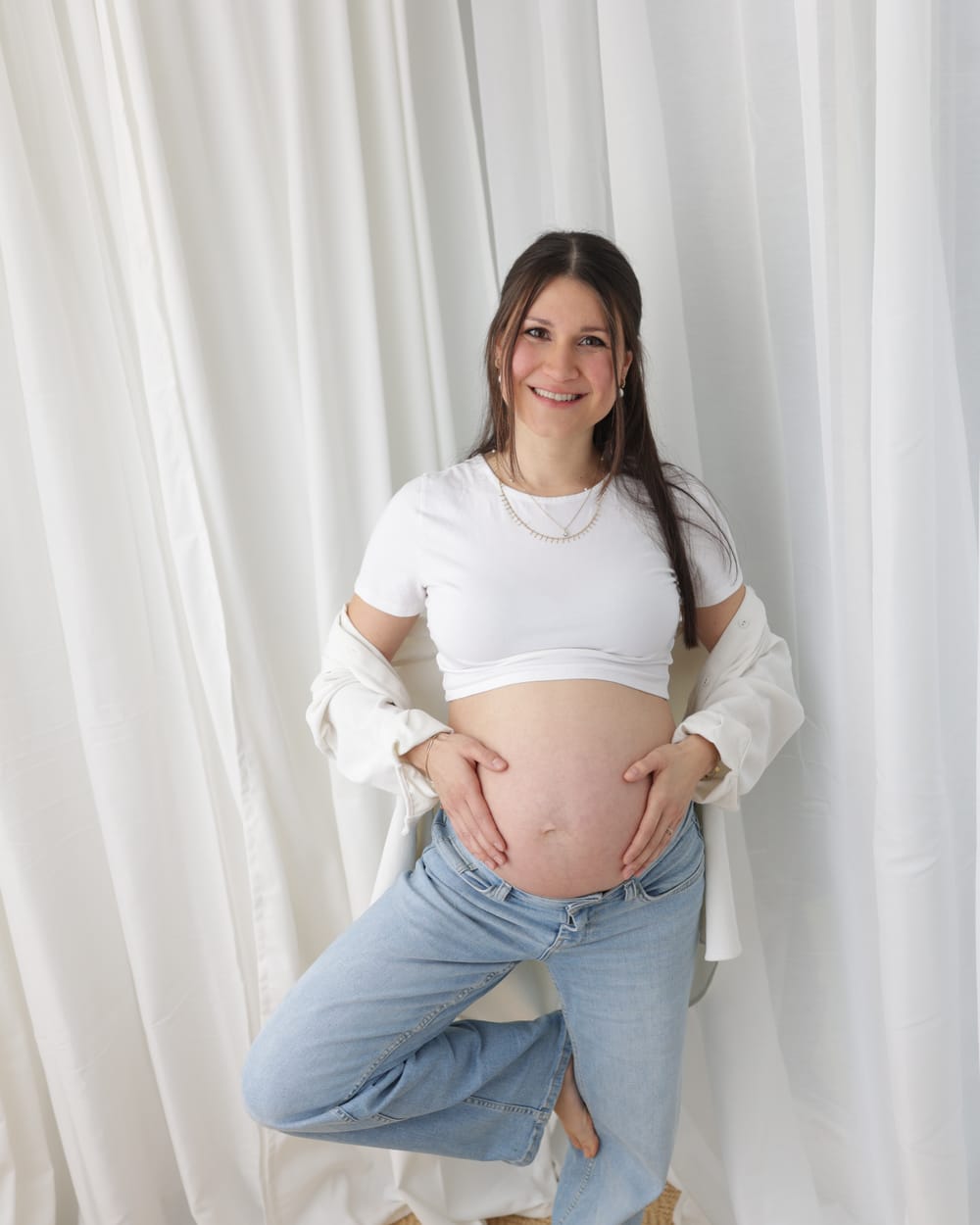 Aylin, schwanger, steht lächelnd und hält ihren Babybauch
