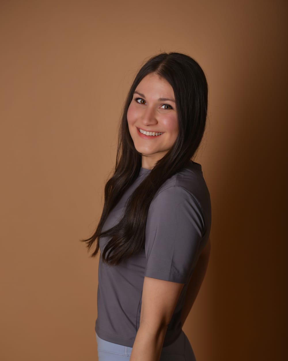Aylin, Trainerin von Lini Mama Fitness, steht lächelnd vor warmem Hintergrund